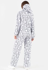 Dwuczęściowy strój w jasnoszarym kolorze z dużymi, wyraźnymi tekstowymi wzorami. Bluza z kapturem ma sznurek do regulacji; spodnie mają luźny krój i elastyczne mankiety.