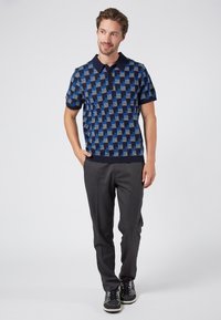 Sininen ja tummansininen neulepaito, jossa on geometrinen kuosi, lyhyet hihat ja kaulus, yhdistetty harmaisiin housuihin ja mustiin tennareihin.