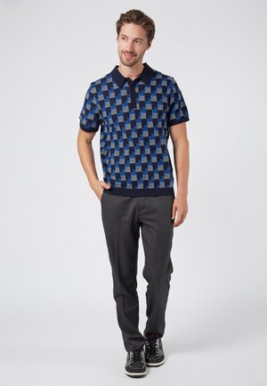 Gesticktes Blau- und Marineblau-Poloshirt mit geometrischem Muster, kurzen Ärmeln und Kragen, kombiniert mit grauen Hosen und schwarzen Sneakers.