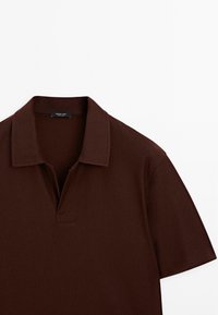 Brun polotröja med kort placket och krage. Tyget har ett strukturerat mönster. Korta ärmar med en ren, minimal design.