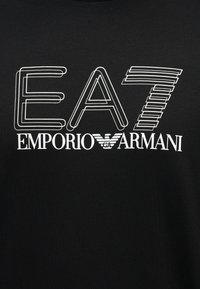 Λογότυπο EA7 με περίγραμμα πάνω από το κείμενο Emporio Armani, με ένα στυλιζαρισμένο σύμβολο αετού σε λευκό σε μαύρο φόντο.