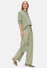 Hellgrüne Bluse mit subtiler Schimmer, kombiniert mit weiten, strukturierten hellgrünen Hosen. Abgerundet mit einer passenden Handtasche und grünen Slippers.