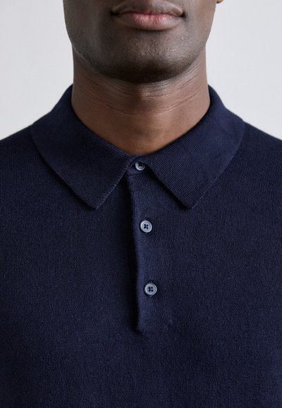 Mörkblå polo skjorta med en mjuk textur, en klassisk krage och tre rundade knappar, som visar en ren och enkel design.