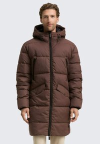 Braune Daunenjacke mit Kapuze, ausgestattet mit einem Reißverschluss auf der Vorderseite, zwei Reißverschlusstaschen auf der Brust und zwei aufgesetzten Taschen auf der Vorderseite. Strukturierte Steppdesign.