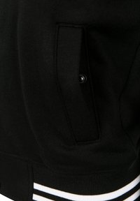 Zwarte sweatshirt met een voorkantzak met een zilveren drukknop. De zoom heeft een geribbelde structuur met witte en gouden strepen.