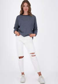 Maglietta a strisce blu navy e bianca a maniche lunghe, abbinata a jeans bianchi strappati e sneakers bianche. Design semplice, vestibilità rilassata e strappi visibili.