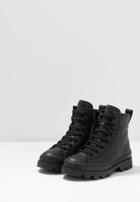 Bottines noires en cuir avec une finition texturée, bout rond, lacets à l'avant et semelles en caoutchouc épaisses avec des bandes prononcées.