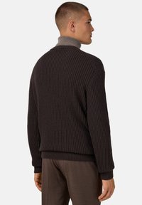 Pull en maille marron foncé avec un motif texturé, doté d'un col haut et de poignets côtelés, porté sur un pantalon marron.