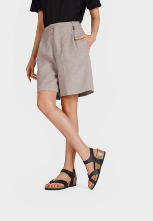 Pantaloni bermuda beige chiaro a vita alta con pieghe e tasche laterali, abbinati a sandali neri con cinturini e tacco a zeppa glitterato.