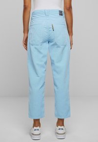 Pantaloni in velluto a coste blu chiaro con gamba dritta, dotati di due tasche posteriori e un piccolo dettaglio a loop multicolore sulla cintura.