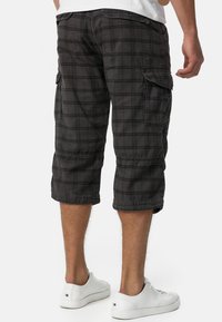 Shorts cargo noirs à motif check, de longueur genou, avec poches latérales et coupe décontractée, assortis à des baskets blanches.