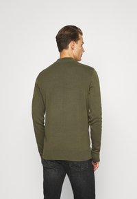 Suéter de punto verde oliva con cuello redondo, mangas largas y dobladillo acanalado. Presenta una textura suave y un diseño ajustado.