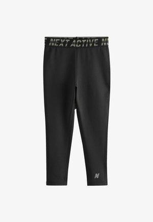 Zwarte sportleggingen met een brede, gemusterde tailleband met de tekst "NEXT ACTIVE" en een klein logo op het onderbeen aan de linkerkant. Glad, rekbaar materiaal.