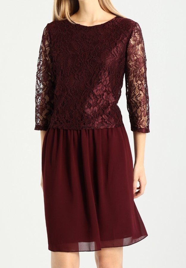 Bordeauxklänning med en spetsöverdelsdel som har trekvartslånga ärmar och en flödande chiffongkjol, som visar upp intrikata blommönster i spets.