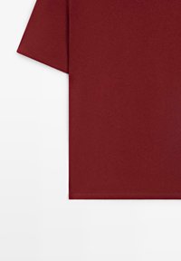 T-shirt bordeaux à manches courtes avec ourlet droit, montré de la taille à la manche sur un fond blanc.