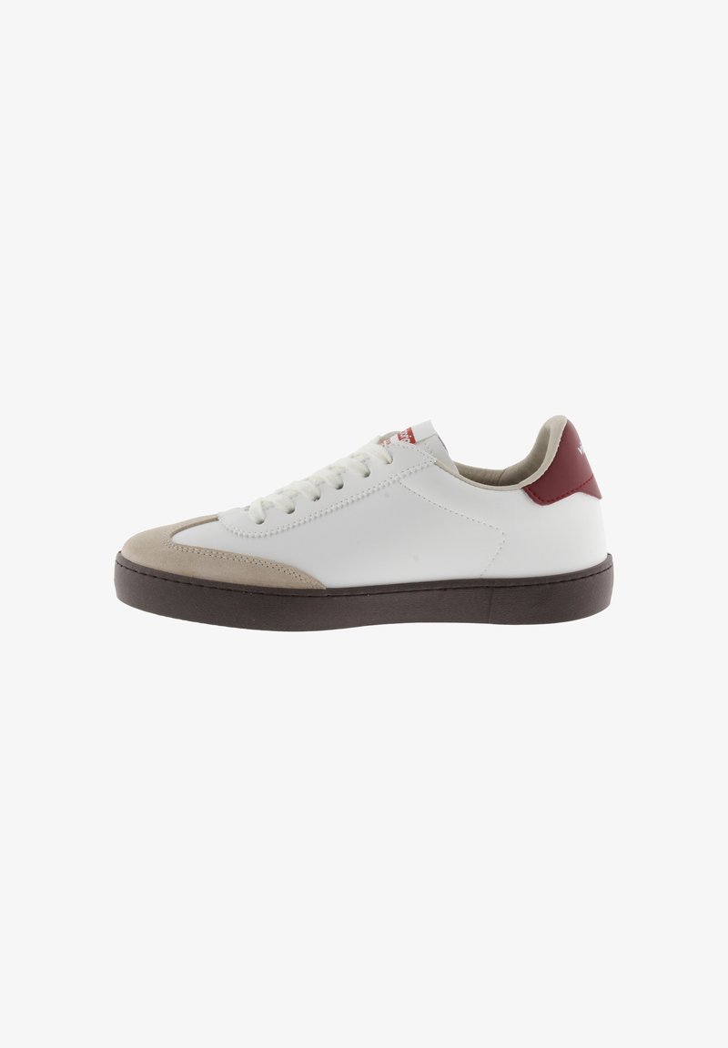 Sneaker bianca con punta in suede beige, suola in gomma marrone e accento rosso sul tallone. Presenta lacci piatti e tomaia in pelle testurizzata.