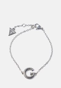 Bracciale in catena argentata con un distintivo charm a forma di "G" con accenti in strass e un tag triangolare "Guess", chiuso con un moschettone.
