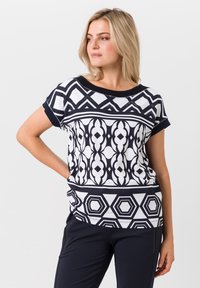 Korte mouwen top met een geometrisch zwart-wit patroon, met zeshoeken en krommingen. Zacht materiaal met een comfortabele pasvorm en zwarte afwerking.