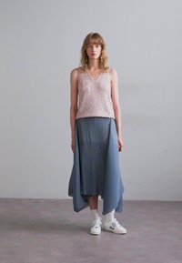 Top rosa chiaro con paillettes e scollo a V, abbinato a una gonna plissettata blu asimmetrica e sneakers bianche. Texture morbide, vestibilità rilassata.