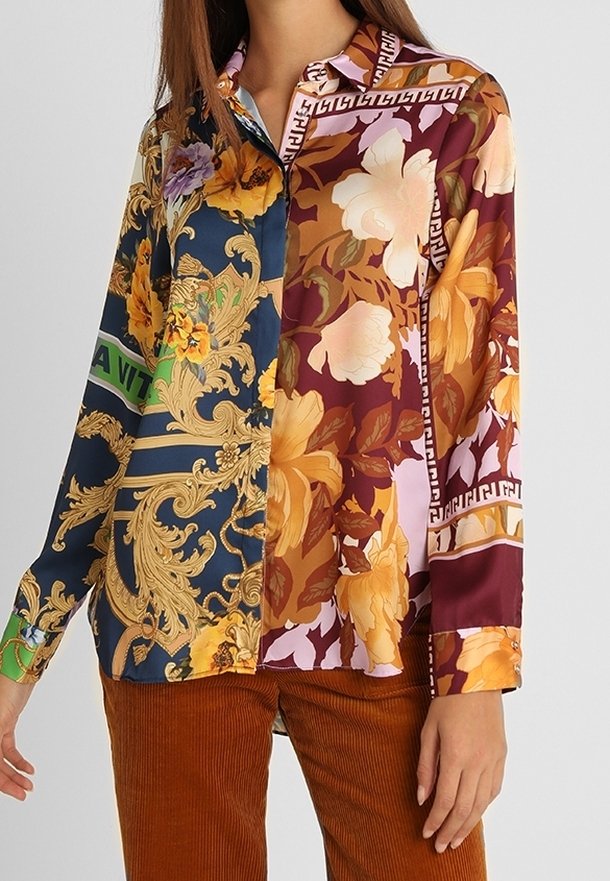 Femme portant une chemise à manches longues boutonnée avec des motifs floraux et baroques mélangés dans des tons bleus, jaunes, bordeaux et orange.