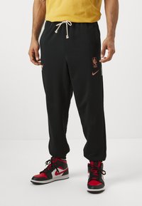 Melnas sporta bikses ar regulējamu auklu, NBA logs un Nike zīmols. Valkā ar sarkaniem un melniem augstpapēžu sneakeriem.