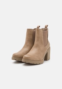 Bottines beiges en cuir lisse, avec des panneaux latéraux élastiques et un talon carré massif. Dos texturé pour plus de détail.