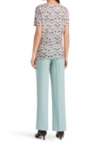 Mujer vistiendo una blusa corta de manga con un patrón rosa y pantalones anchos de mezclilla azul claro, de pie de espaldas, con zapatos de tacón negros.