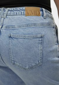 Ljust blå denim jeans med en läderlapp som visar "VMD" på baksidan av linningen; har en enda bakficka med sömnadsdetaljer.