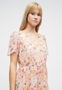 Φλοράλ φόρεμα σε ανοιχτό ροζ ύφασμα, με κοντά φουσκωτά μανίκια, V-λαιμόκοψη και ζωνάκι με κορδόνι στη μέση, με ανάμεικτα πολύχρωμα λουλουδάτα σχέδια.