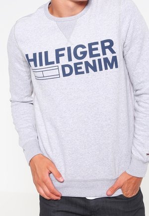 Grijze sweatshirt met lange mouwen, ronde hals en een groot blauw "HILFIGER DENIM" logo op de voorkant. Voorzien van ribgebreide manchetten en zoom.