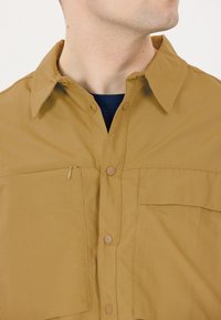 Beige overhemd met knoopsluiting en een gespreide kraag, voorzien van twee borstzakken en een ritszakdetail. Lichtgewicht, gestructureerde stof met een gladde afwerking.