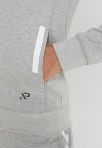 Sudadera gris con franjas de acento blancas, bolsillos laterales, puños acanalados, detalle de logo en el dobladillo y tejido suave y texturizado.
