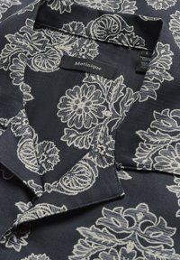Maglietta blu navy con motivo floreale e paisley bianco, con colletto e etichetta del brand. Tessuto testurizzato con dettagli di cucitura.