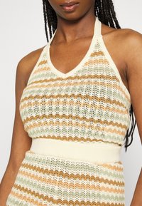 Strick-Haltertop mit V-Ausschnitt, alternierenden Streifen in Grün, Orange und Beige sowie einem gerippten Taillenbund für zusätzliche Textur.