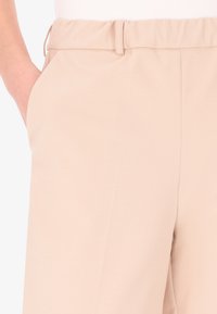 Pantaloni beige con vita arricciata, tasche laterali e una morbida trama di tessuto liscia. Design classico con una vestibilità rilassata.