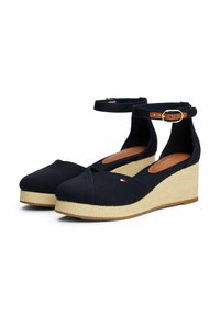 Marineblaue Leinenschuhe mit Keilabsatz und Knöchelriemchen, ausgestattet mit einer geflochtenen Jutesohle und einem kleinen Logodetail an der Seite. Glatte Stofftextur.