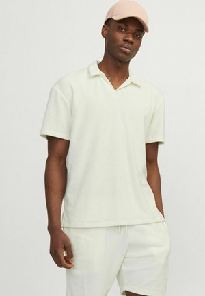 Polo shirt giallo chiaro a maniche corte con vestibilità rilassata, caratterizzato da un colletto a v e una trama morbida. Abbinato a pantaloni corti coordinati.