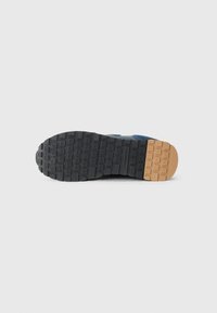 De zool van de sneaker heeft een gegoten zwarte rubberen onderkant met een gepatternde grip en een lichtbruine sectie bij de hiel, ontworpen voor grip.
