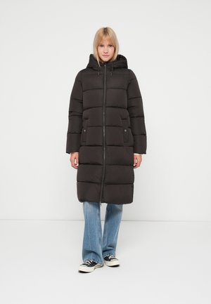 Sort pufferjakke med hætte, der har en frontlynlås, trykknaplommer og horisontal quiltning. Kombineret med blå jeans og sneakers.