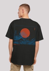 Juoda marškinėliai su dideliu mėlynos bangos dizainu ir raudonos saulės grafika ant nugaros, o apačioje yra japonų kalba raudona.