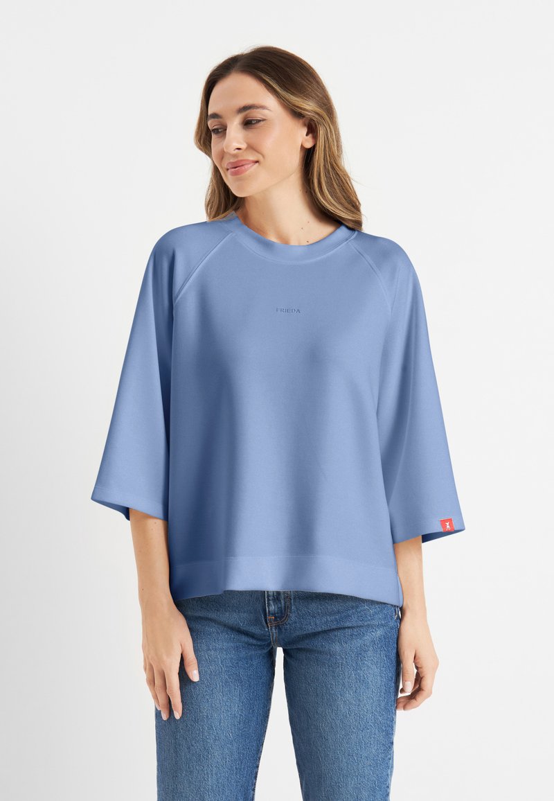 Lichtblauwe sweatshirt met een ronde halslijn, raglanmouwen en een klein logo op de borst; heeft een rood etiket op de mouw.