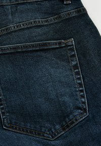 Dark blue denim jeans, featuring a back pocket with a distinctive stitched design and subtle texture, showcasing a classic straight fit.