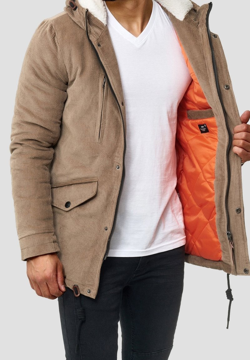 Hellbraune Cordjacke mit einem pelzgefütterten Kapuzen, einer orangen gesteppte Innenfutter, Vordertaschen und einem Reißverschlussverschluss.