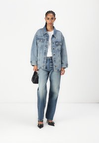 Lys blå denimjakke, løs passform med krage og frontlommer. Kombinert med høyt midjejeans og svarte spisse hæler. Svart håndveske inkludert.