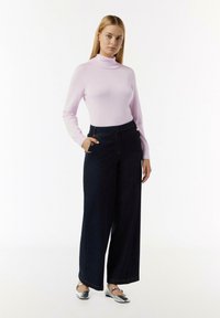 Hellrosa Rollkragenpullover, dunkelblaue weite Jeans mit goldenen Knopfakzenten und silbernen Ballerinas. Glattes Material und strukturierte Passform.