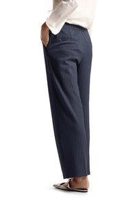 Pantalons rayés navy en tissu lisse, avec une coupe décontractée, des poches latérales et une ceinture épurée, associés à des chaussures plates à enfiler.