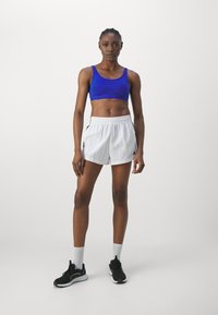 Niebieski stanik sportowy, białe spodenki z czarnymi akcentami, czarne buty sportowe i białe skarpetki do kostki. Gładkie tkaniny, sportowy design.