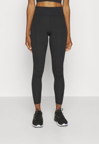 Zwarte leggings van rekbaar materiaal met een hoge taille, een gladde textuur en een slim fit, gecombineerd met zwarte sportschoenen.