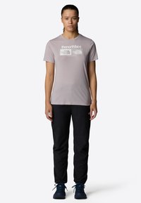 Camiseta de manga corta de color gris claro con el logo "the north face", combinada con pantalones negros y botas de senderismo azules, llevada por un individuo de pie.