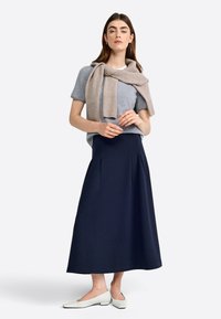 T-shirt gris, pull beige clair drapé sur les épaules, jupe midi plissée bleu marine et chaussures plates blanches. Tenue simple et décontractée.